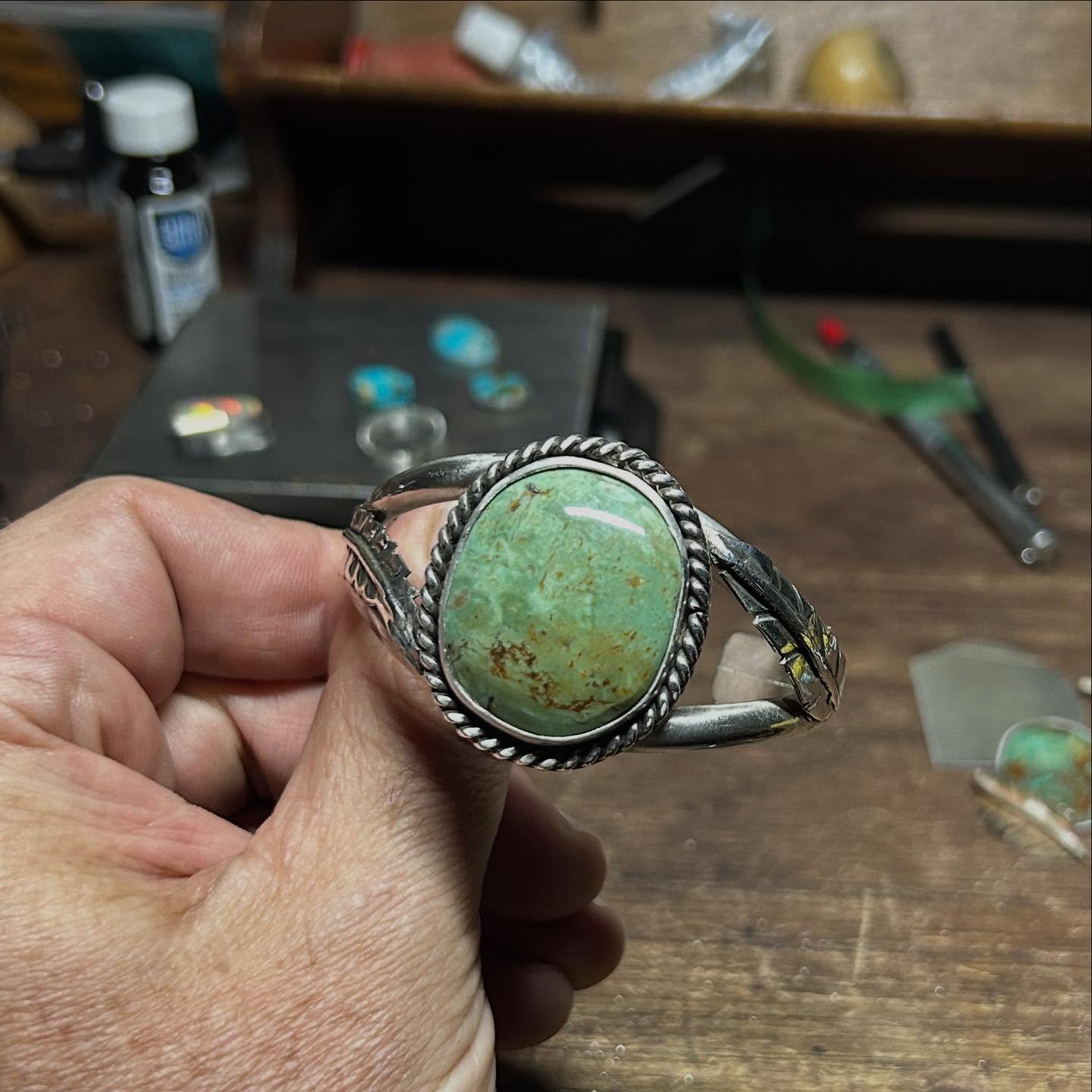 Kingman Hardy Pit turquoise cuff with rope bezel and silver feather detail, in the maker's hand at the bench